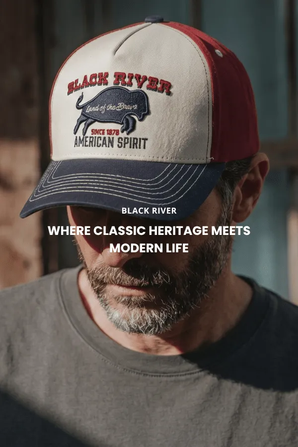 Ein Mann sitzt auf einer Holzkiste in einem Studio und trägt einen klassischen braunen Cowboyhut aus Filz mit breiter Krempe, ein dunkles Denimhemd und Jeans.